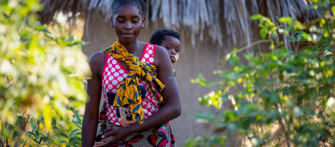 A woman outside carrying her baby on her back