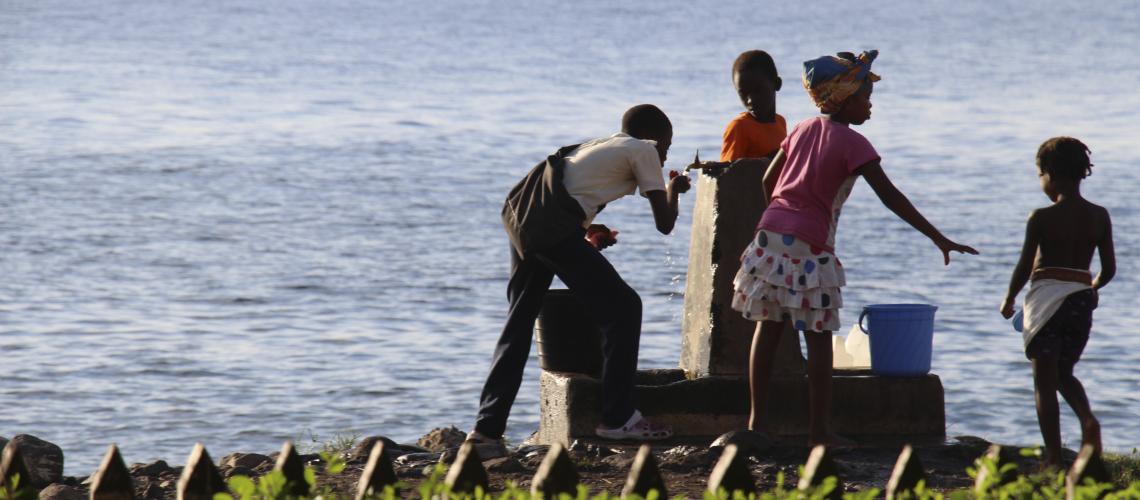 A group of children at a drinking fountain with a water body in the background