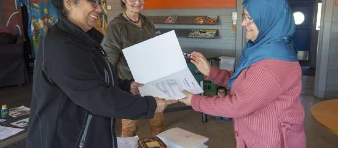 A woman giving paper to another woman in blue burkha