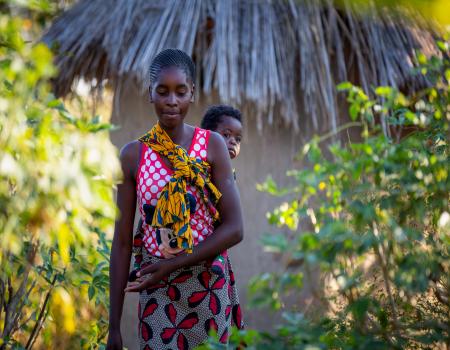 A woman outside carrying her baby on her back